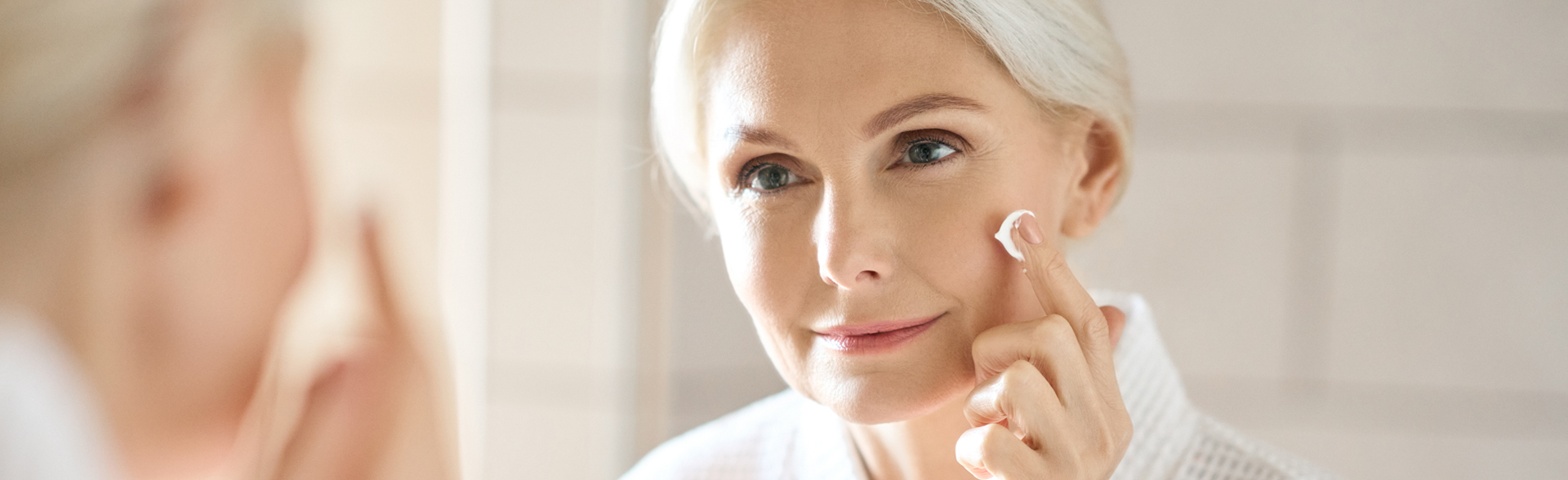 Nahaufnahme einer Frau mit weißen Haaren, die Creme auf ihr Gesicht aufträgt.